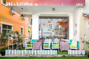 An outdoor seating area with tables and chairs, a white picket fence, and a view of buildings through a glass door. - Miss You Guesthouse (Shenzhen)