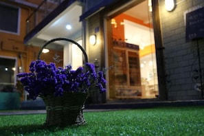 A wicker basket with purple flowers on artificial grass in front of a building with a glass entrance. - Miss You Guesthouse (Shenzhen)