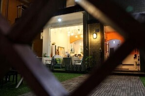 Un espacio de comedor al aire libre con mesas y sillas, un muro de ladrillo y un reloj en la pared.