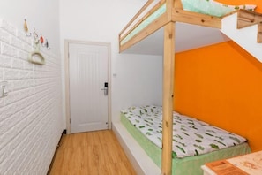 A room with a bunk bed, a white door, a white brick wall, and an orange accent wall.