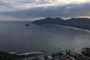 Vista costera con barandilla, una masa de agua y montañas distantes.