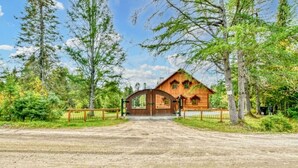 A rustic wooden cabin with a dirt driveway leading to a gated entrance, surrounded by dense forest. - The Escapade - Private hot tub with pool table 6BR (Sainte-Lucie-des-Laurentides)
