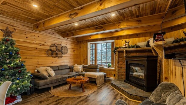 A cozy cabin interior with a wooden interior, a fireplace, a Christmas tree, and a sofa. - The Escapade - Private hot tub with pool table 6BR (Sainte-Lucie-des-Laurentides)