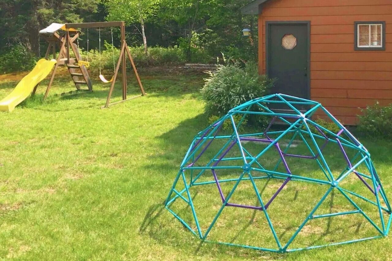 A backyard with a swing set, a slide, and a geodesic dome structure.