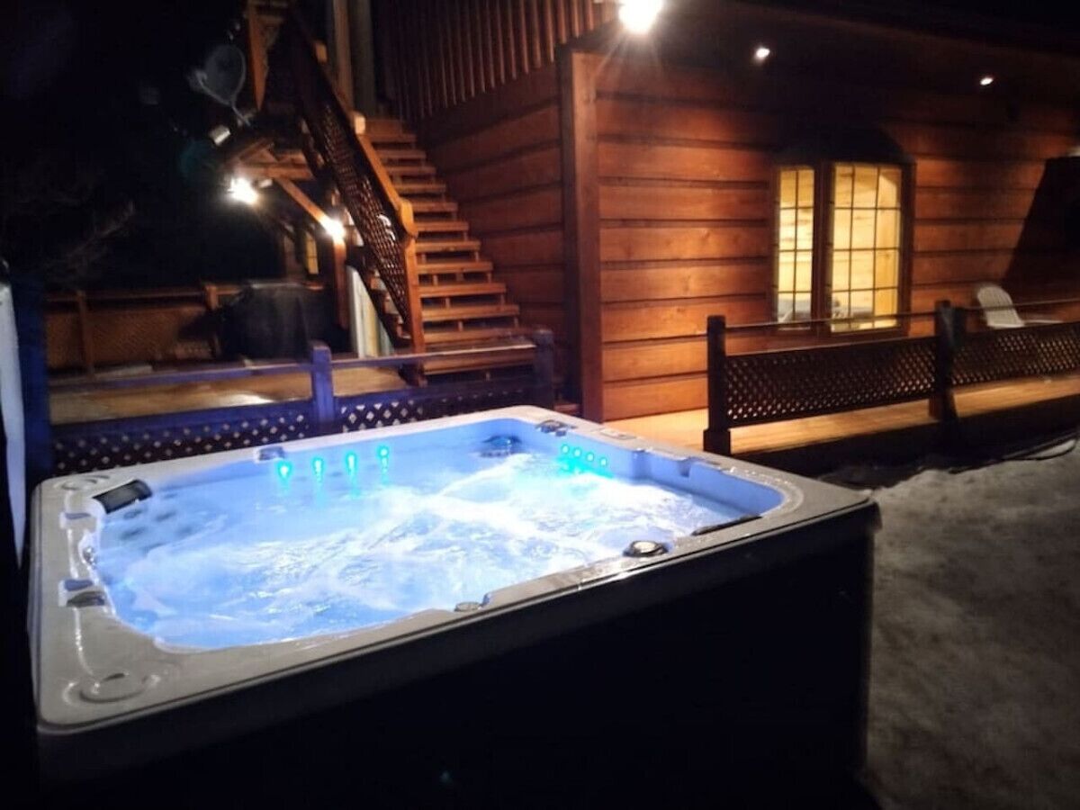 A hot tub with a wooden deck and stairs leading to a cabin.