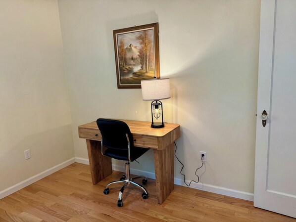Ein Holztisch mit einem schwarzen Bürostuhl, einer Lampe und einem Bild an der Wand.