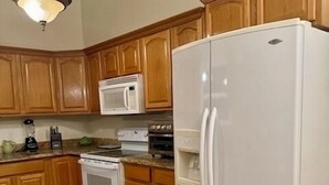 Una cocina con armarios de madera, un refrigerador blanco, una estufa, un microondas y una lámpara colgante.