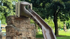 Un parque infantil con un tobogán sobre base de piedra, rodeado de árboles y césped.