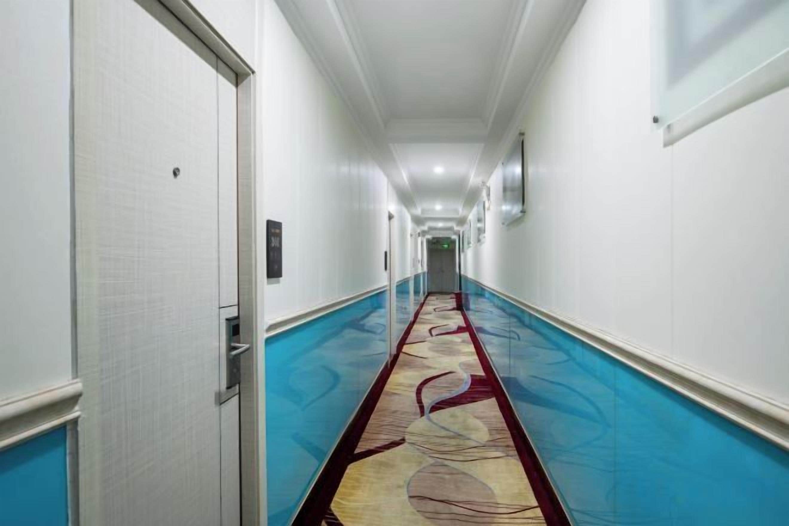 A hotel corridor with a patterned carpet, white walls, and doors on either side.