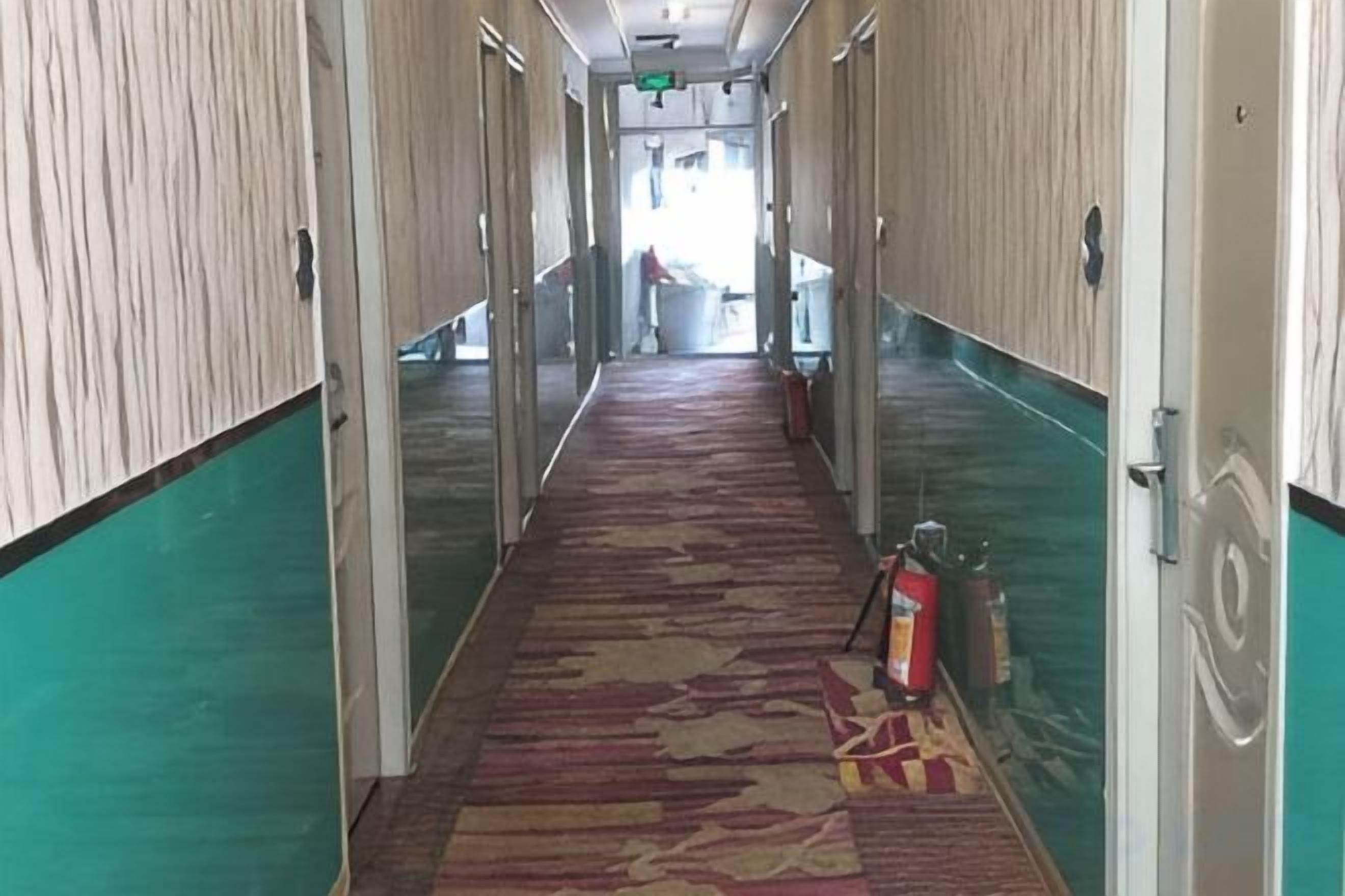 Un corridoio di un hotel con tappeto a motivi, porte in vetro e un estintore sul pavimento.