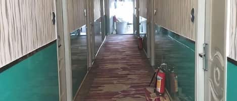 A hotel corridor with a patterned carpet, glass doors, and a fire extinguisher on the floor.