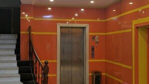 An elevator with a metallic interior, a staircase with black railings, and a red wall with yellow stripes. - Seven Orange Hotel (Shenzhen Yannan Metro Station Huaqiang North Branch) (Shenzhen)