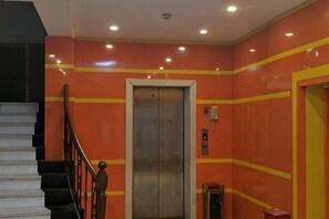 An elevator with a metallic interior, a staircase with black railings, and a red wall with yellow stripes. - Seven Orange Hotel (Shenzhen Yannan Metro Station Huaqiang North Branch) (Shenzhen)