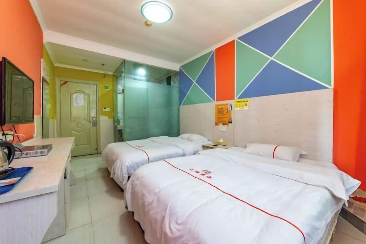 A hotel room with two beds, a desk with a computer, and a bathroom with a mirror.