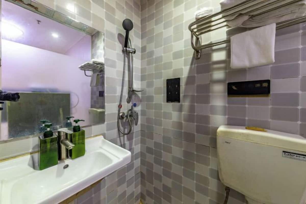 A bathroom with a white sink, green soap dispensers, a handheld showerhead, a towel rack, and a toilet.
