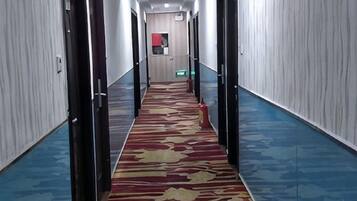 A hotel corridor with a patterned carpet, doors on both sides, and a blue floor.