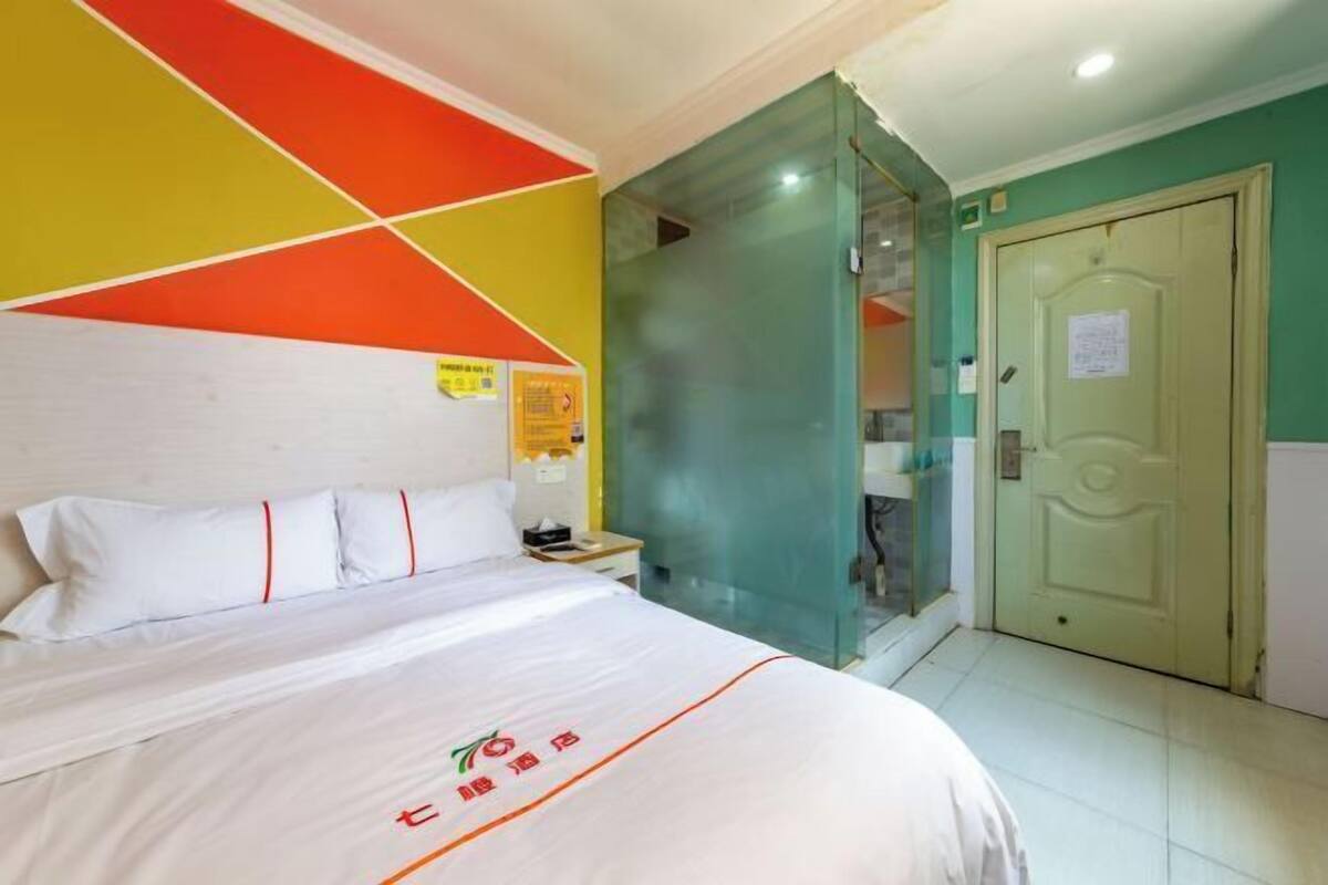 A hotel room with a bed, a nightstand, a glass partition, and a door.