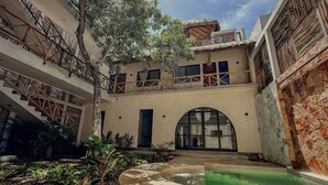 A courtyard with a pool, a tree, and a building with a thatched roof and wooden balconies. - "Bugambilia" Tulum Deluxe Suite (Tulum)