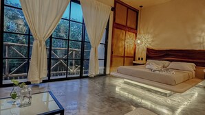 A modern bedroom with a large bed, a glass coffee table, and a view of a forest through large windows. - "Bugambilia" Tulum Deluxe Suite (Tulum)