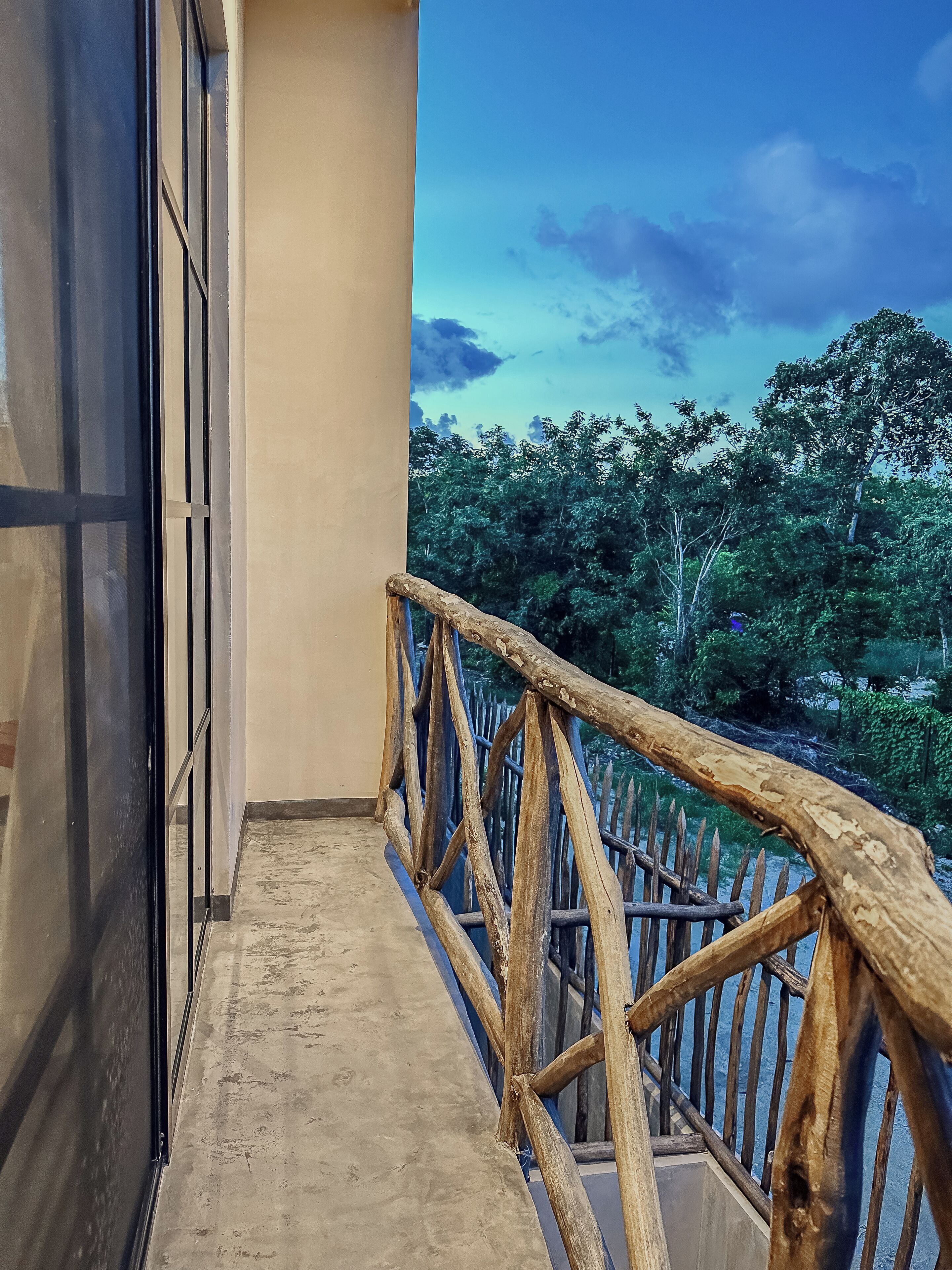 Un balcon doté d’une balustrade en bois, donnant sur une zone boisée.