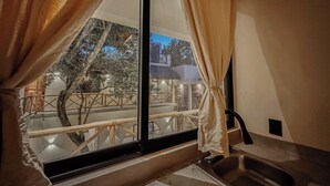 A room with a large window, a sink, and a view of an outdoor area with trees and a building. - "Bugambilia" Tulum Deluxe Suite (Tulum)
