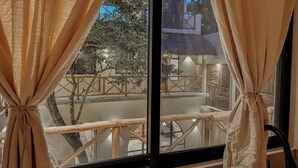 A room with a large window, curtains, and a view of an outdoor area with a wooden deck and a building. - "Bugambilia" Tulum Deluxe Suite (Tulum)