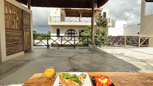 A dining table with a meal and a glass of orange juice on a terrace with a view of a building and a gate. - "Lapislázuli" Premium exotic Suite with private pool (Tulum)