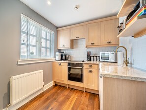 Une cuisine moderne avec des meubles en bois, un four encastré, un four à micro-ondes et une fenêtre avec des stores.