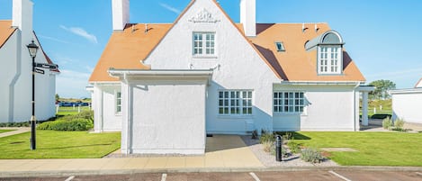 A white building with a brown roof, a covered entrance, and a parking lot in front.