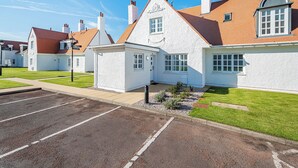 A white building with a red roof, a small attached structure, and a parking lot. - Lundin Links - UKC6916 (Turnberry)