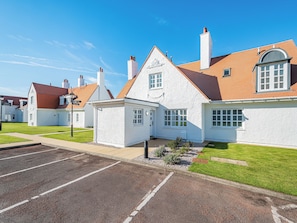 A white building with a red roof, a small attached structure, and a parking lot. - Lundin Links - UKC6916 (Turnberry)