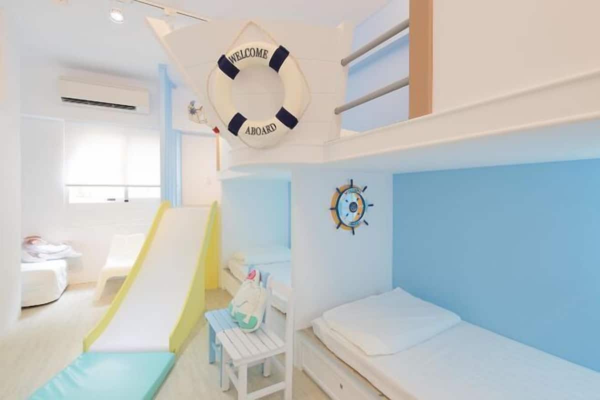 A bunk room with a bunk bed, a slide, a small table, and a life preserver decoration.