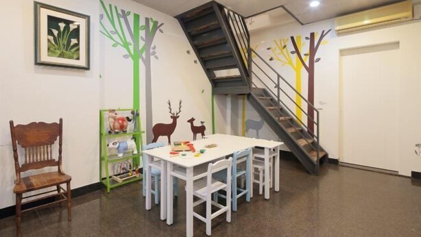 A children's playroom with a table, chairs, a bookshelf, and a staircase. - Xigang Waipojia (Tainan)