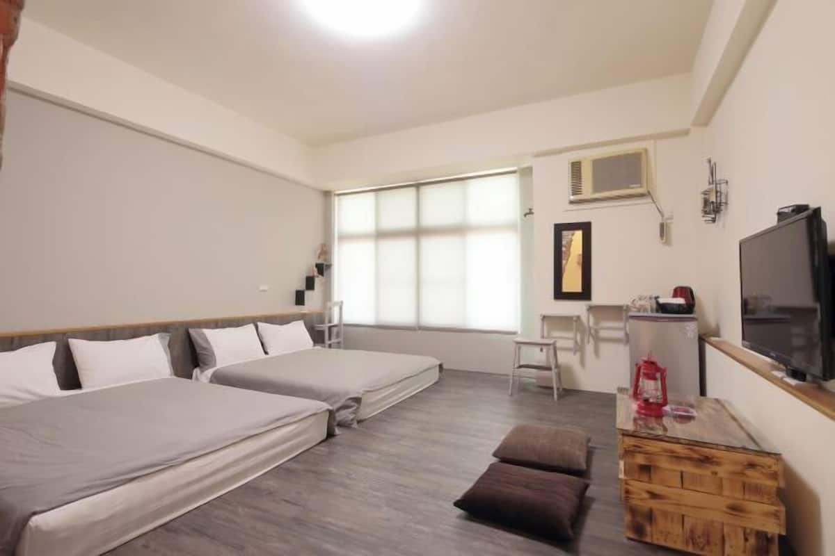 A room with two beds, a television, a desk, and a window with blinds.