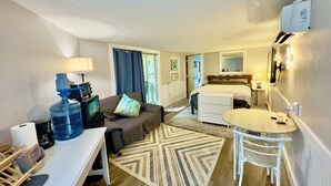 Ein kleines Hotelzimmer mit einem Bett, einem kleinen Schreibtisch, einem Stuhl, einem Wasserspender, einem Fernseher und einem Fenster mit Vorhängen.