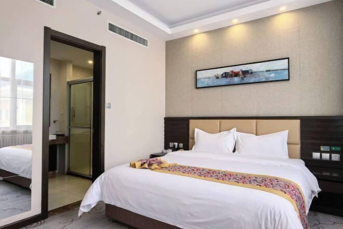 A hotel room with a bed, a nightstand, a painting, and a door leading to another room.