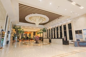 A spacious lobby with a central reception desk, a large chandelier, and several potted plants.
