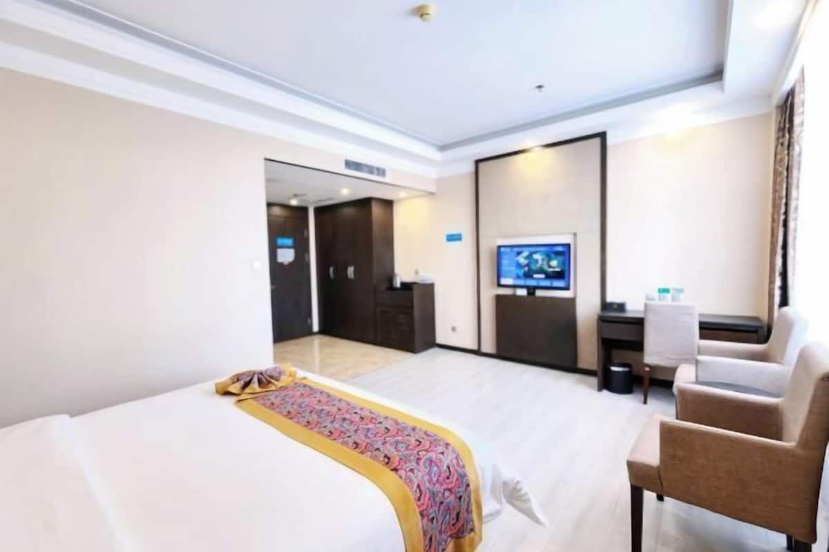 A hotel room with a bed, a desk, a chair, a television, and a door leading to another room.