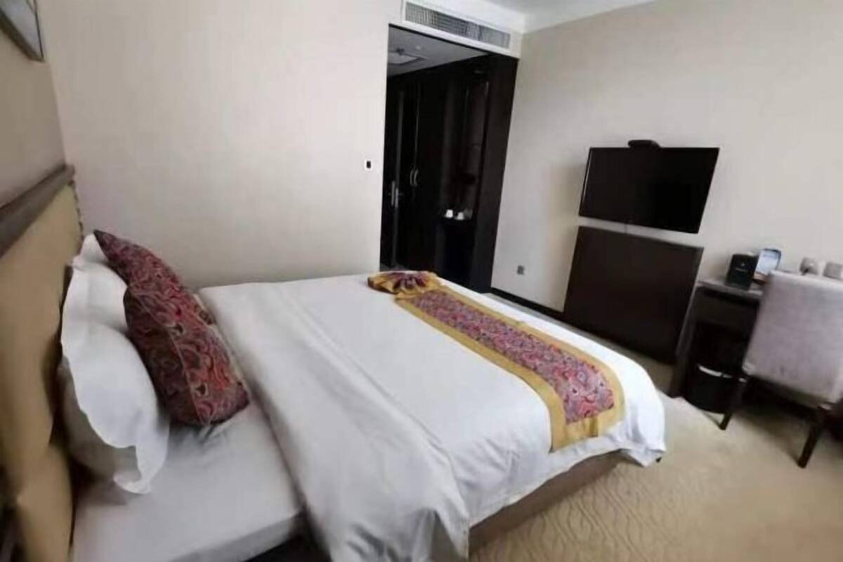 A hotel room with a bed, a desk, a chair, a TV, and a wardrobe.