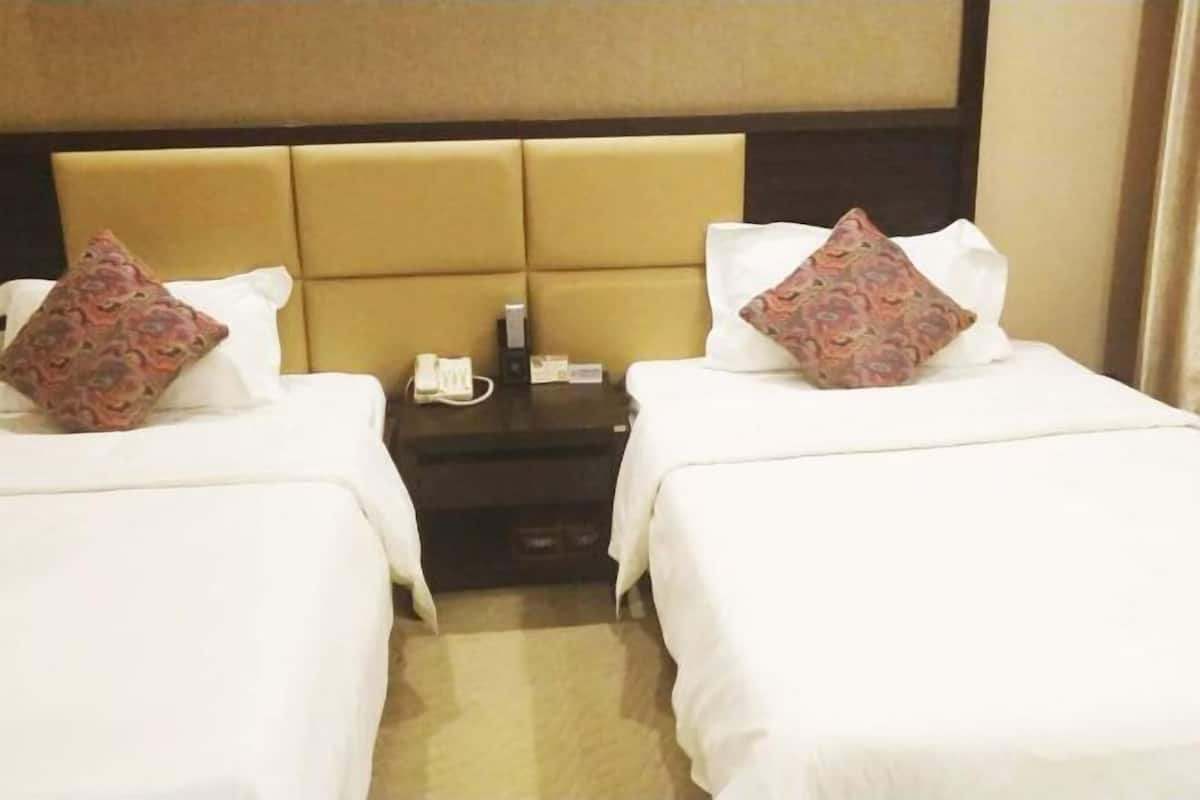 A hotel room with two beds, each with a pillow and a bedside table with a phone and a small item.