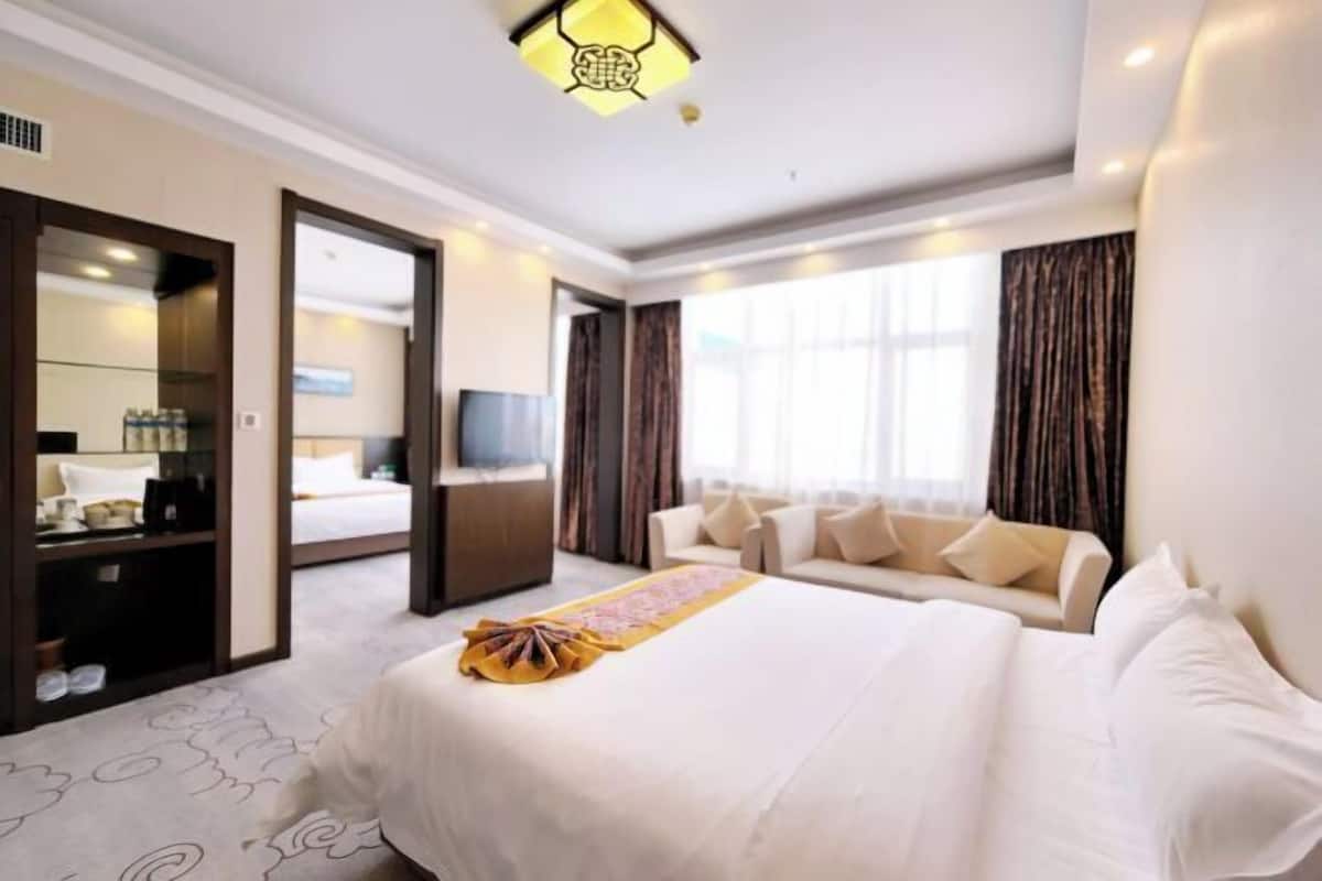 A hotel room with a large bed, a TV, a sofa, and a window with curtains.