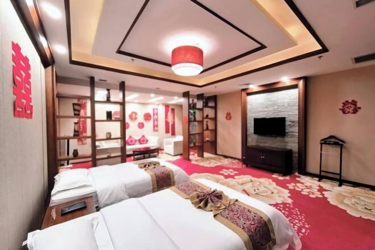 A hotel room with two beds, a TV, a red carpet, and a traditional decor style.