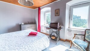 A bedroom with a bed, a dresser, a sewing machine, a chair, and a window with a view of trees.