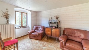 A cozy room with a wooden floor, a brown leather sofa, a wooden cabinet, and a window with a view.