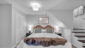 Ein aufgeräumtes Schlafzimmer mit einem großen Bett, zwei Nachttischen, einem Kopfteil und einer Treppe.