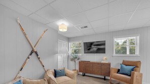 Ein modernes Wohnzimmer mit einer Couch, einem Holzstuhl, einem Kuhfellteppich und Ski, die an der Wand lehnen.