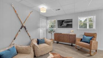 Un salon moderne avec un canapé, une chaise en bois, un tapis en peau de vache et des paires de skis appuyés contre le mur.