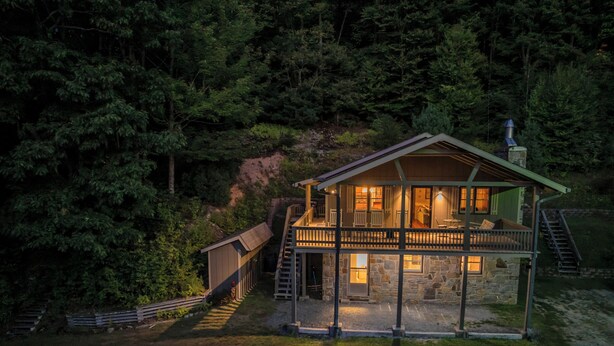 Eine zweistöckige Holzhütte mit Balkon, umgeben von dichtem Wald.