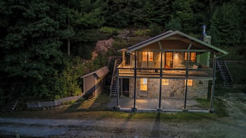 Une cabane à deux étages dotée d’un balcon, entourée d’une forêt dense.