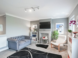 A living room with a grey sofa, a white armchair, a fireplace, a TV, and a bookshelf.